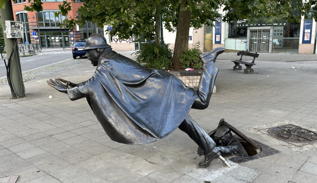 Statue of policeman being tripped by man appearing from manhole